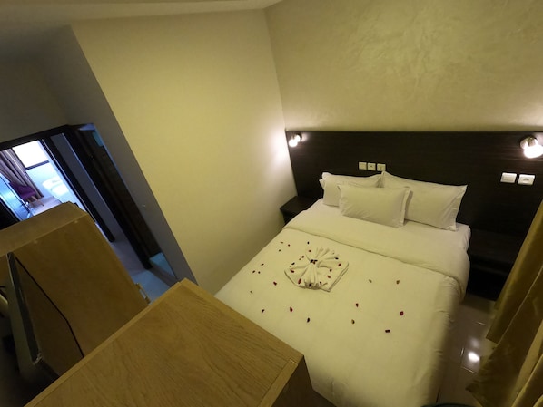 Una habitación de hotel con una cama, mesitas de noche y vistas al pasillo.