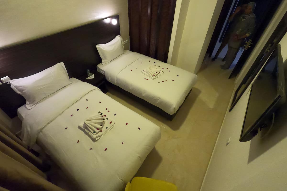 A hotel room with two beds, each with white linens and a decorative towel arrangement.