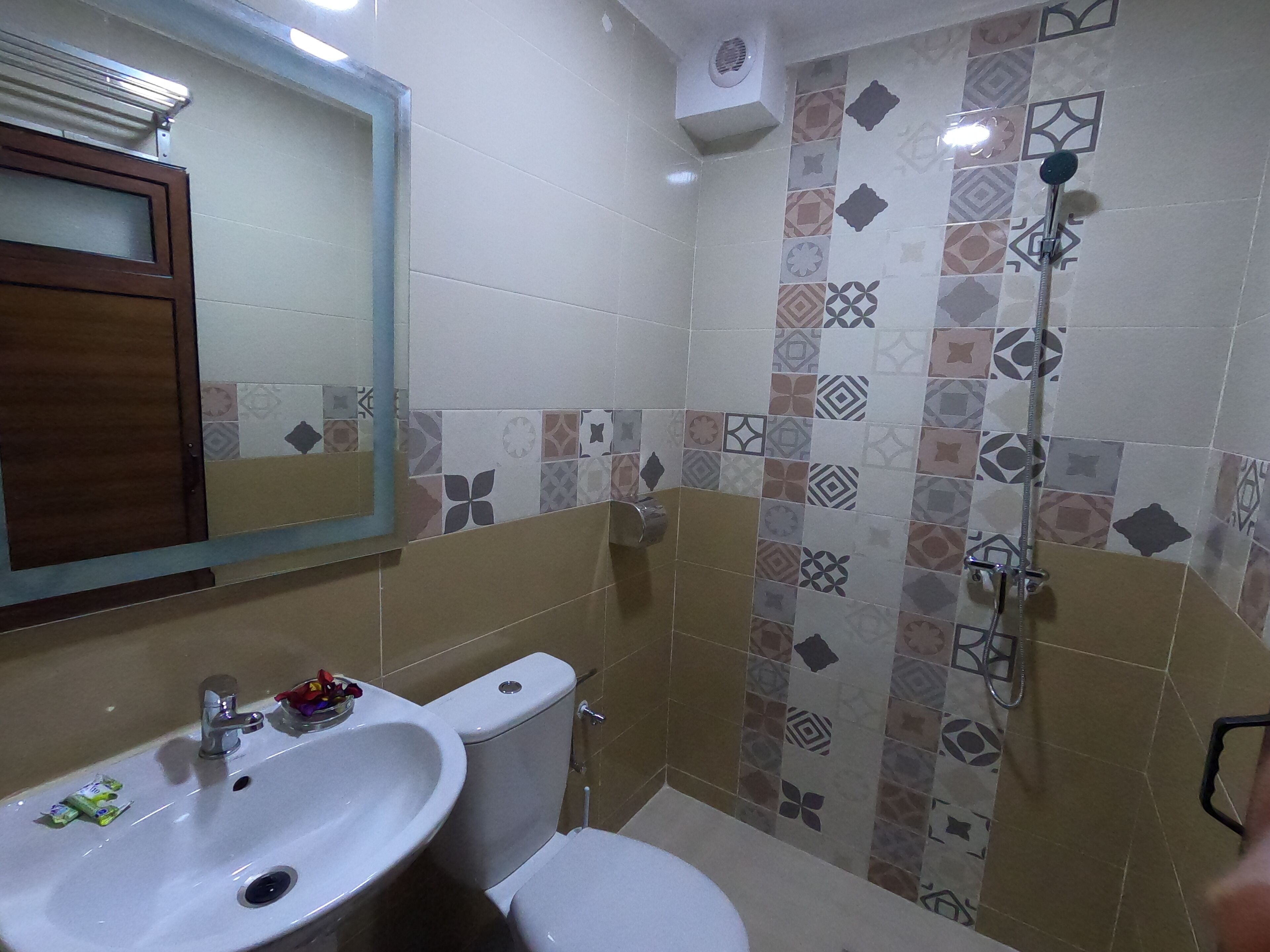 A bathroom with a white sink, toilet, and shower. The walls are tiled with various patterns.