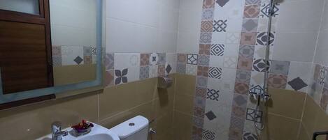 A bathroom with a white sink, toilet, and shower. The walls are tiled with various patterns.