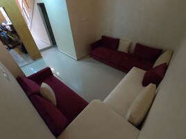 Sala de estar con sofá rojo y color beige, piso de baldosas y una escalera visible que lleva a otra zona.
