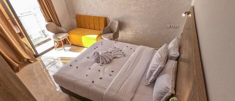 A hotel room with a bed, a small sofa, a wooden headboard, and a view through a window.