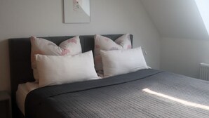 Ein Schlafzimmer mit einem Bett, Kissen, einem gerahmten Bild an der Wand und einem Fenster.