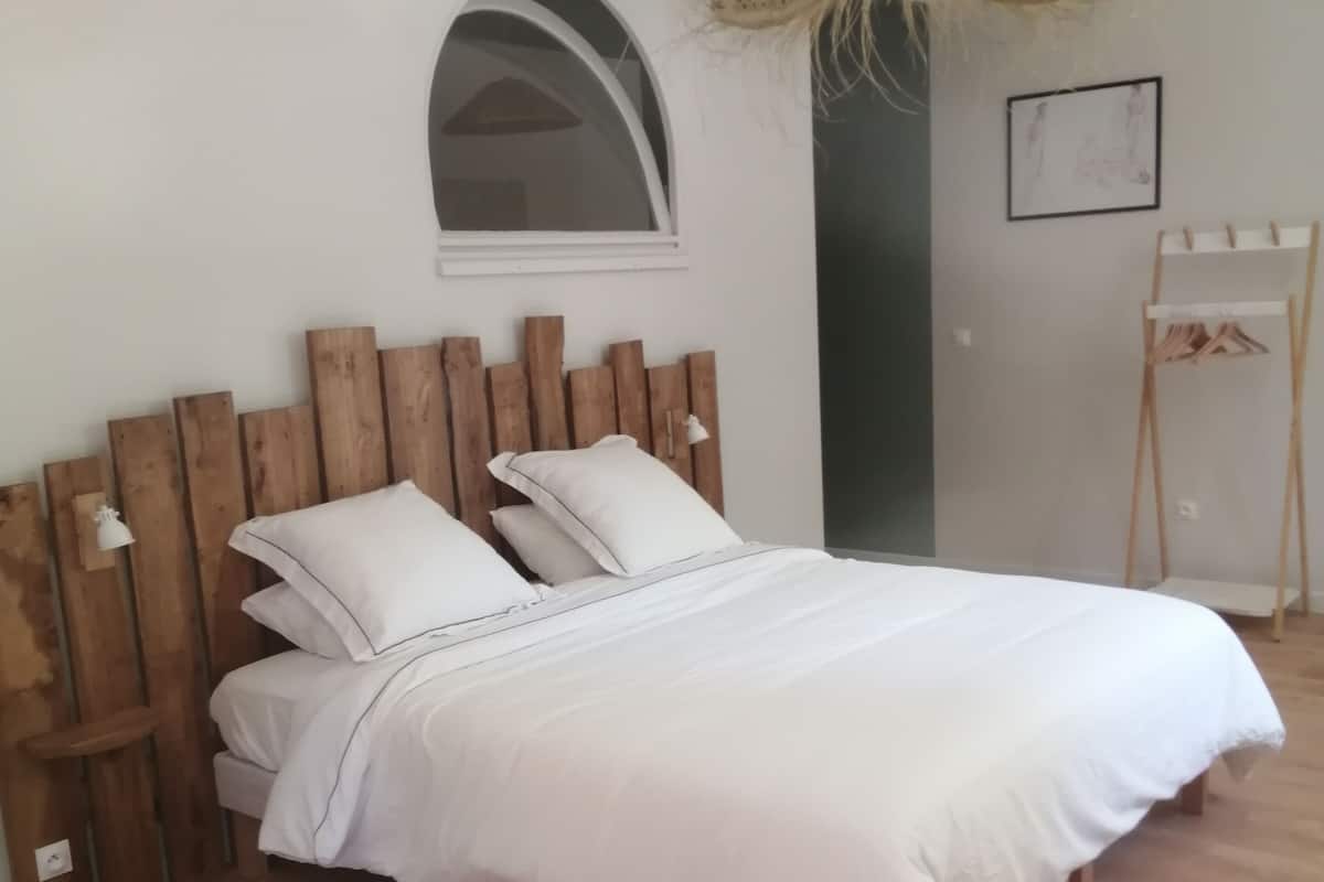 Uma cama com cabeceira de madeira, roupa de cama branca e uma cesta suspensa acima.