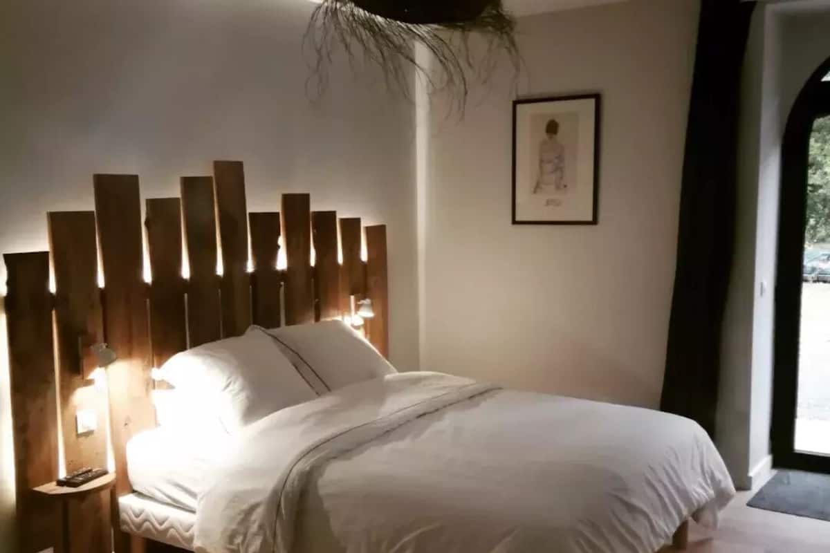 Quarto com cama, cabeceira de madeira, abajures e um quadro na parede.