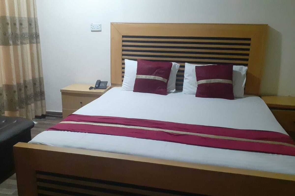 Une chambre avec un lit en bois, une table de chevet avec un téléphone et un fauteuil en cuir noir.