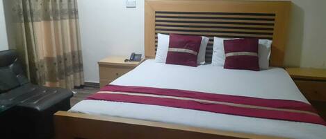 Un dormitorio con una cama de madera, una mesita de noche con un teléfono y un sillón de cuero negro.