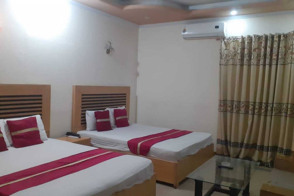 Une chambre d’hôtel avec deux lits, chacun agrémenté de draps rouges et blancs, une petite table et un appareil de climatisation fixé au mur.