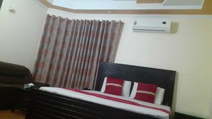 A bedroom with a bed, a dark-colored sofa, a curtain, and an air conditioning unit. - Hotel Pak Inn Gulberg (Lahore)