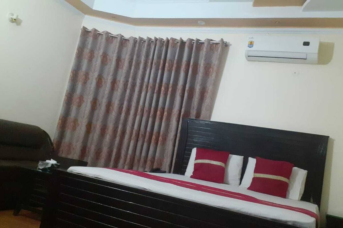 Une chambre à coucher avec un lit, un canapé de couleur sombre, un rideau et un appareil de climatisation.
