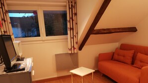 Une pièce chaleureuse avec un plancher en bois, une table blanche sur laquelle repose un livre, un canapé orange et une fenêtre avec des rideaux.