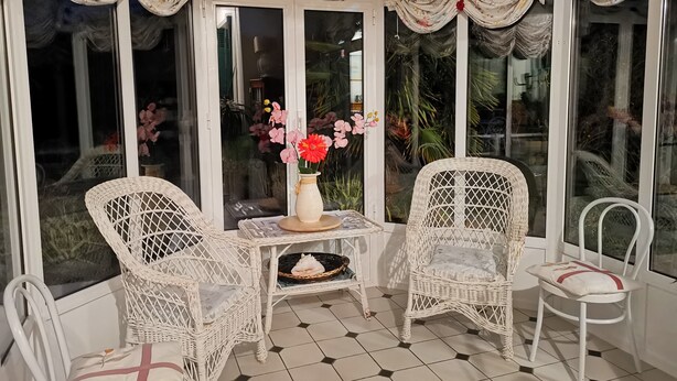 Une véranda avec des fauteuils en osier, une petite table et un vase rempli de fleurs.