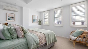 A bedroom with a bed, a chair, and large windows with blinds.