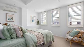 A bedroom with a bed, a chair, and large windows with blinds.