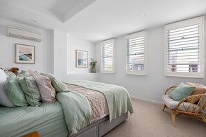 A bedroom with a bed, a chair, and large windows with blinds.