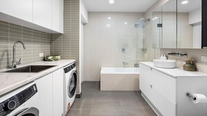 A modern bathroom with a built-in washing machine, a glass-enclosed shower, and a large mirror.