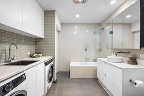 A modern bathroom with a built-in washing machine, a glass-enclosed shower, and a large mirror.