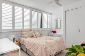 Ein Schlafzimmer mit Bett, Nachttisch, Lampe und einem Fenster mit Jalousien.