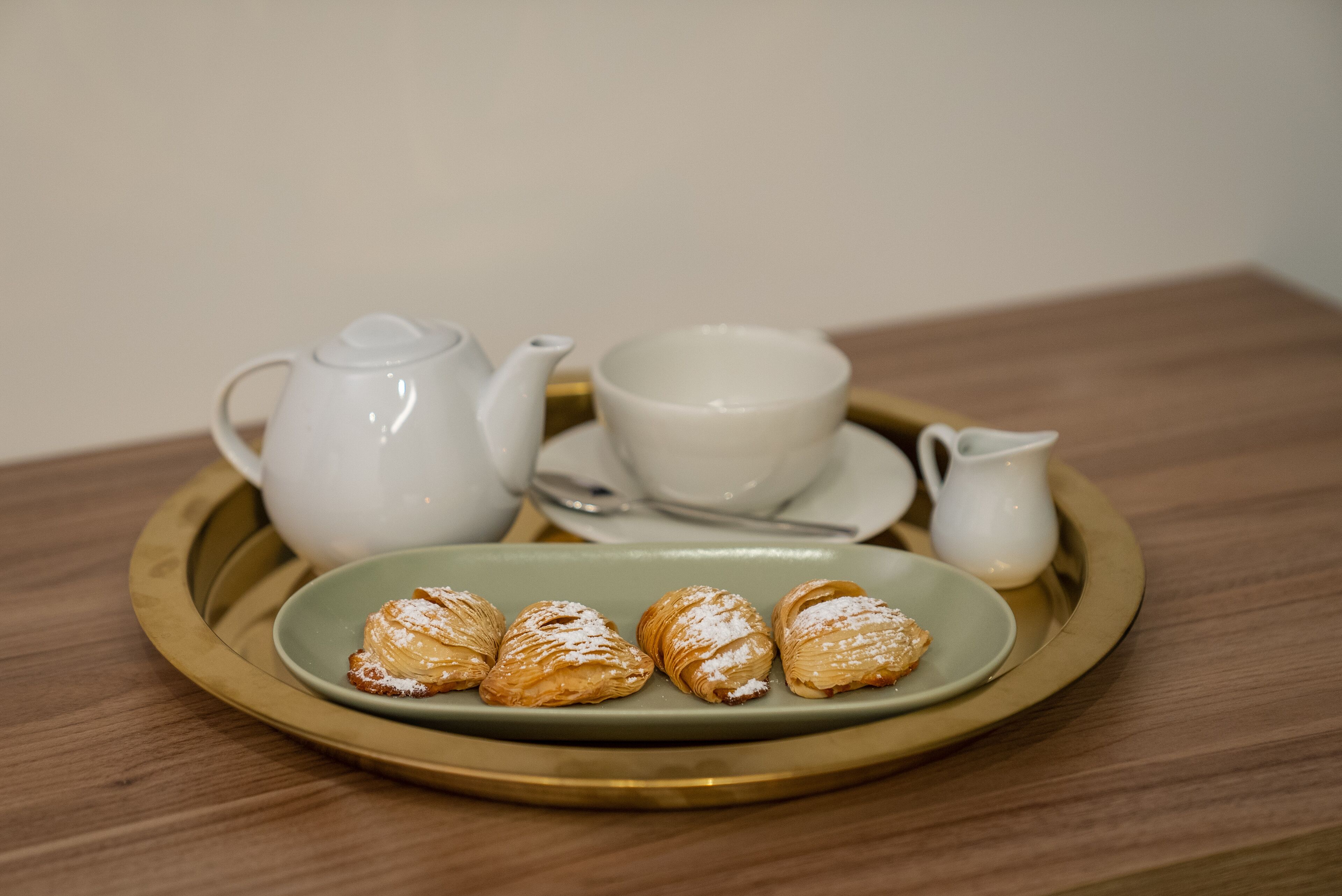 A tray with a teapot, cups, a pitcher, and pastries on a wooden table.