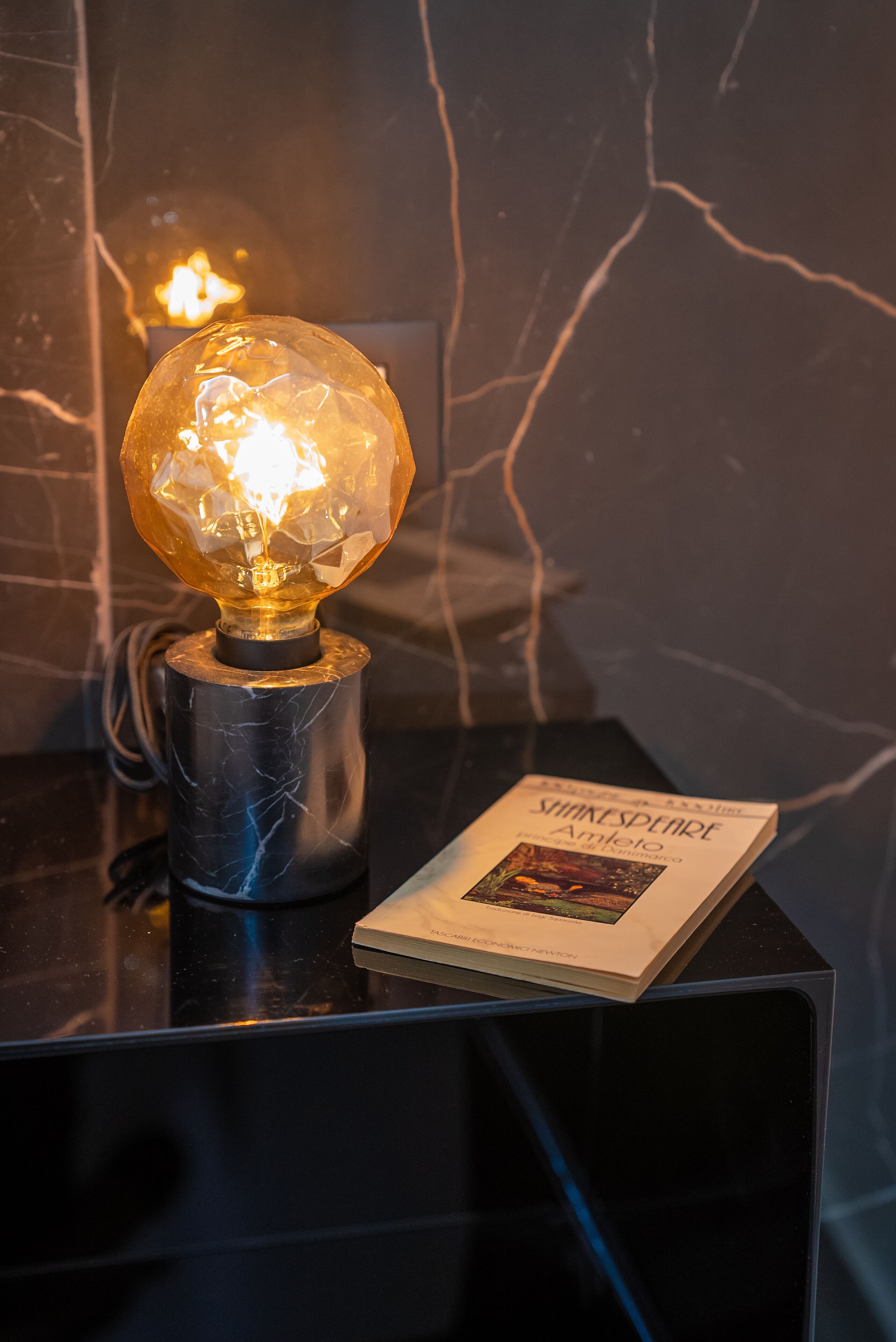 A table with a decorative light fixture and a book titled "Shakespeare's Hamlet" on it.