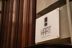 Skilt for 'HAAT Boutique Hotel' monteret på en væg med baggrund af træpaneler.