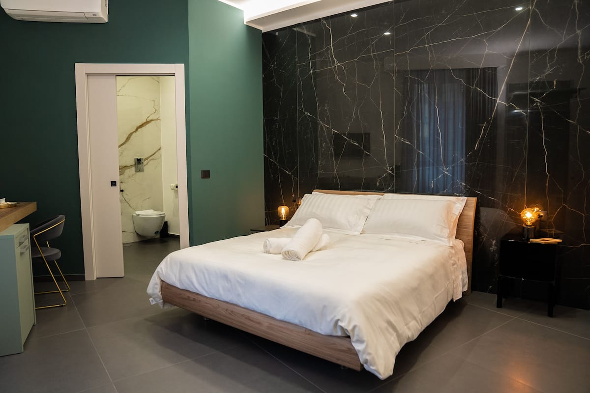 A modern bedroom with a marble-patterned wall, a wooden bed, and a small bedside table with a lamp.