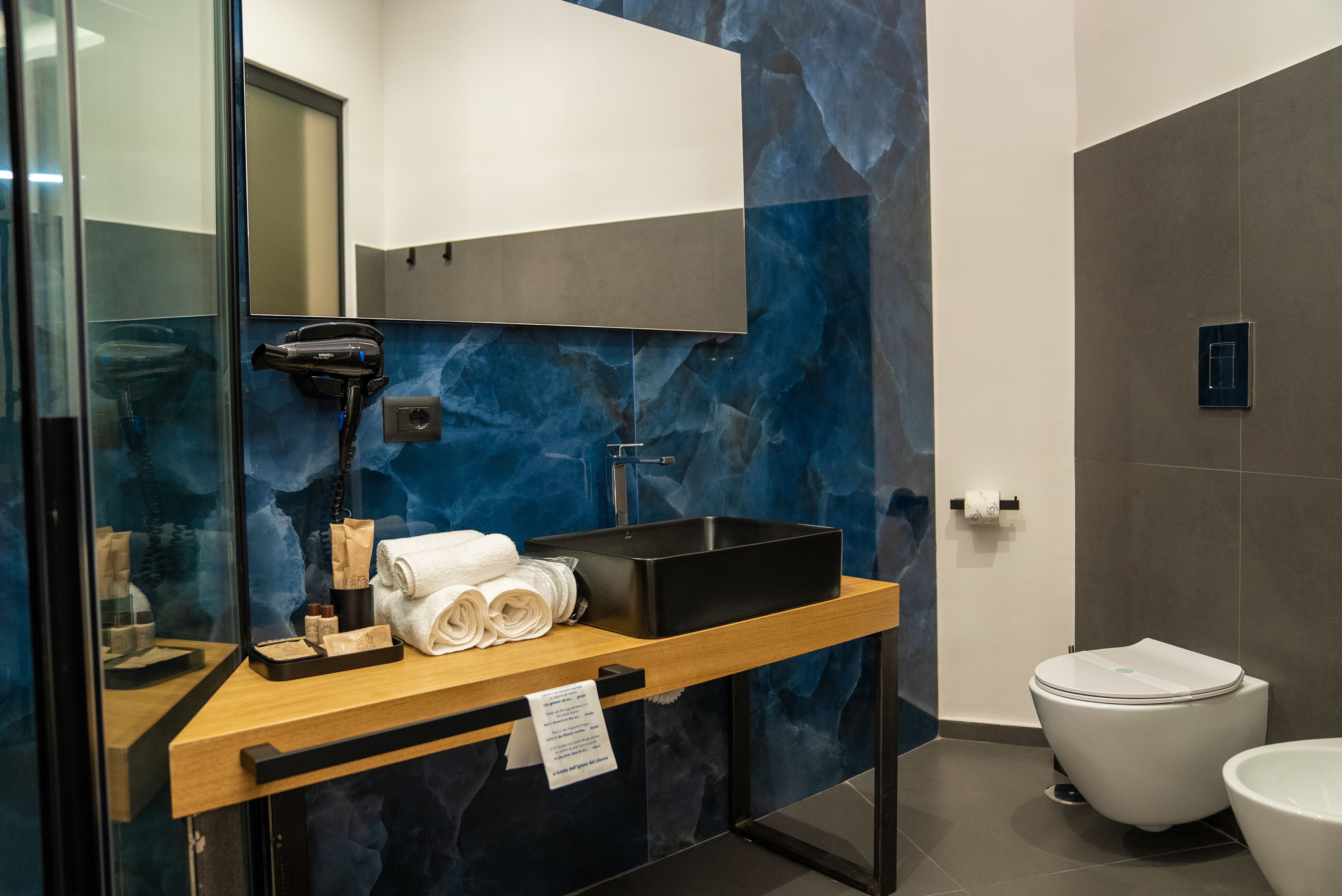 A modern bathroom with a marble backsplash, a wooden vanity, a black sink, and a white toilet.