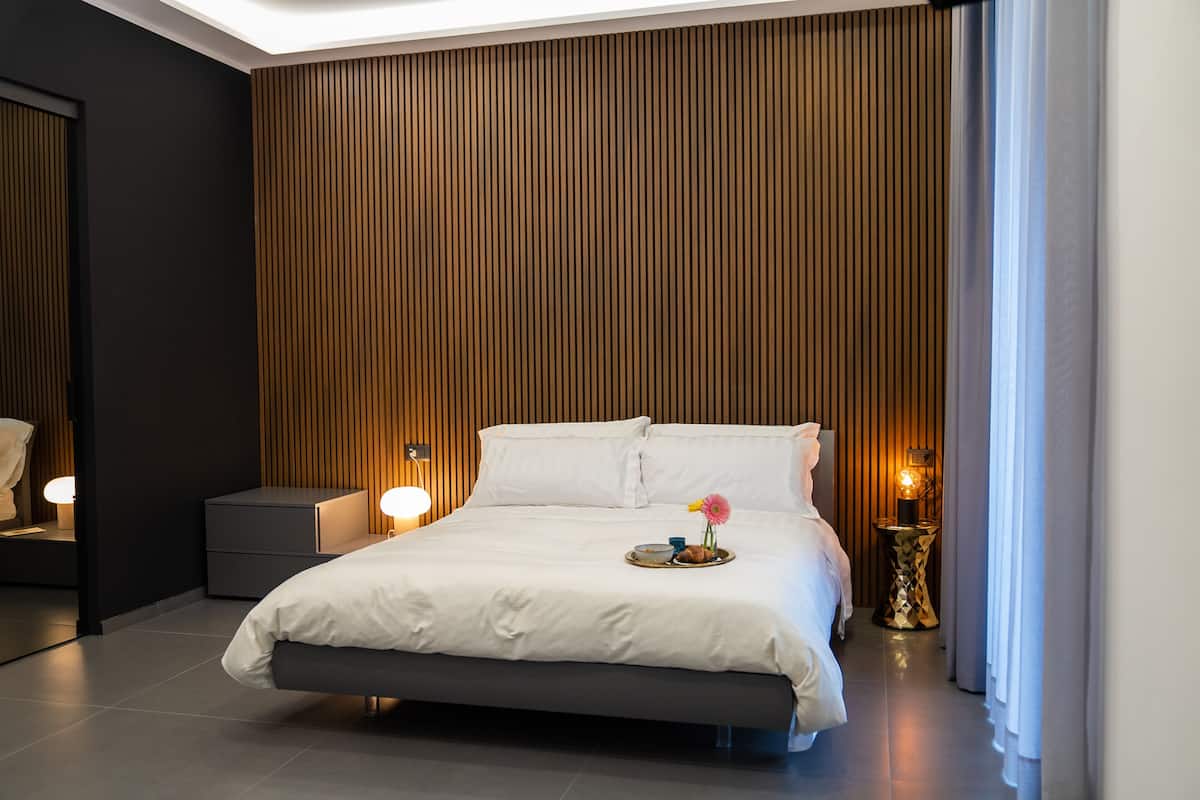 A modern hotel room with a large bed, bedside lamps, a tray with breakfast items, and a decorative flower.