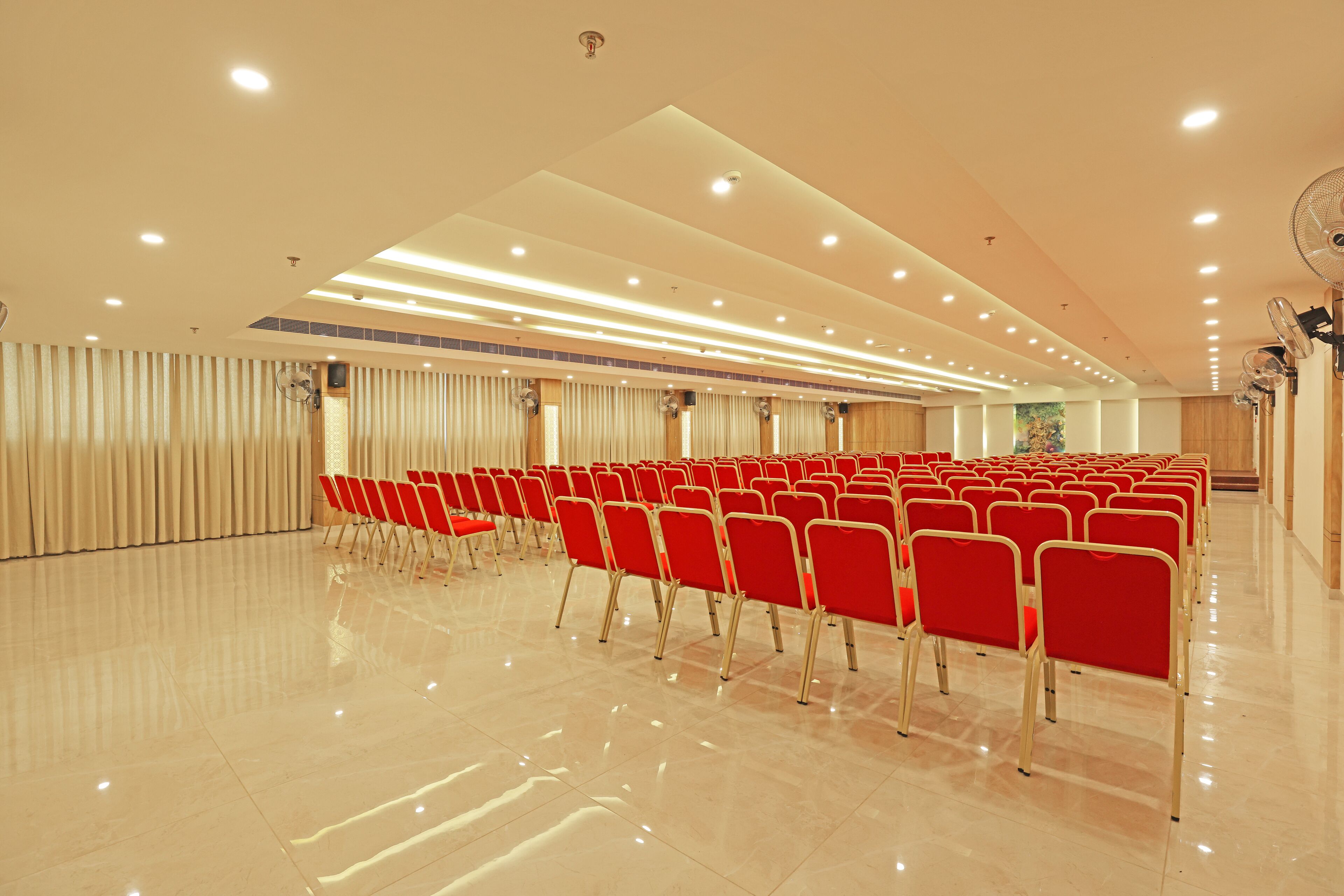A spacious hall with rows of red chairs, a polished floor, and recessed ceiling lighting.