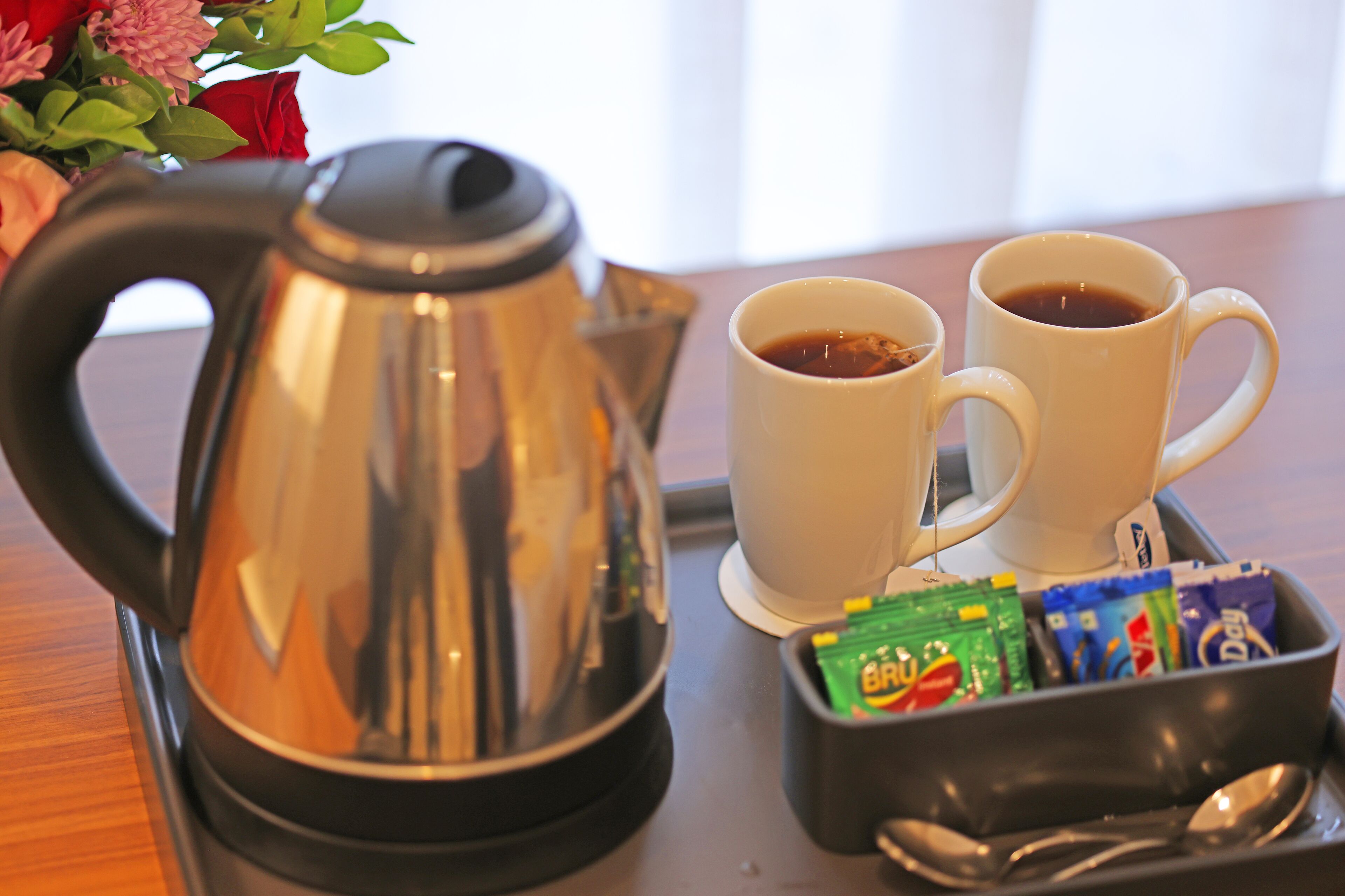Un ensemble pour préparer le café comprenant une bouilloire, deux tasses et un plateau avec des sachets de sucre.