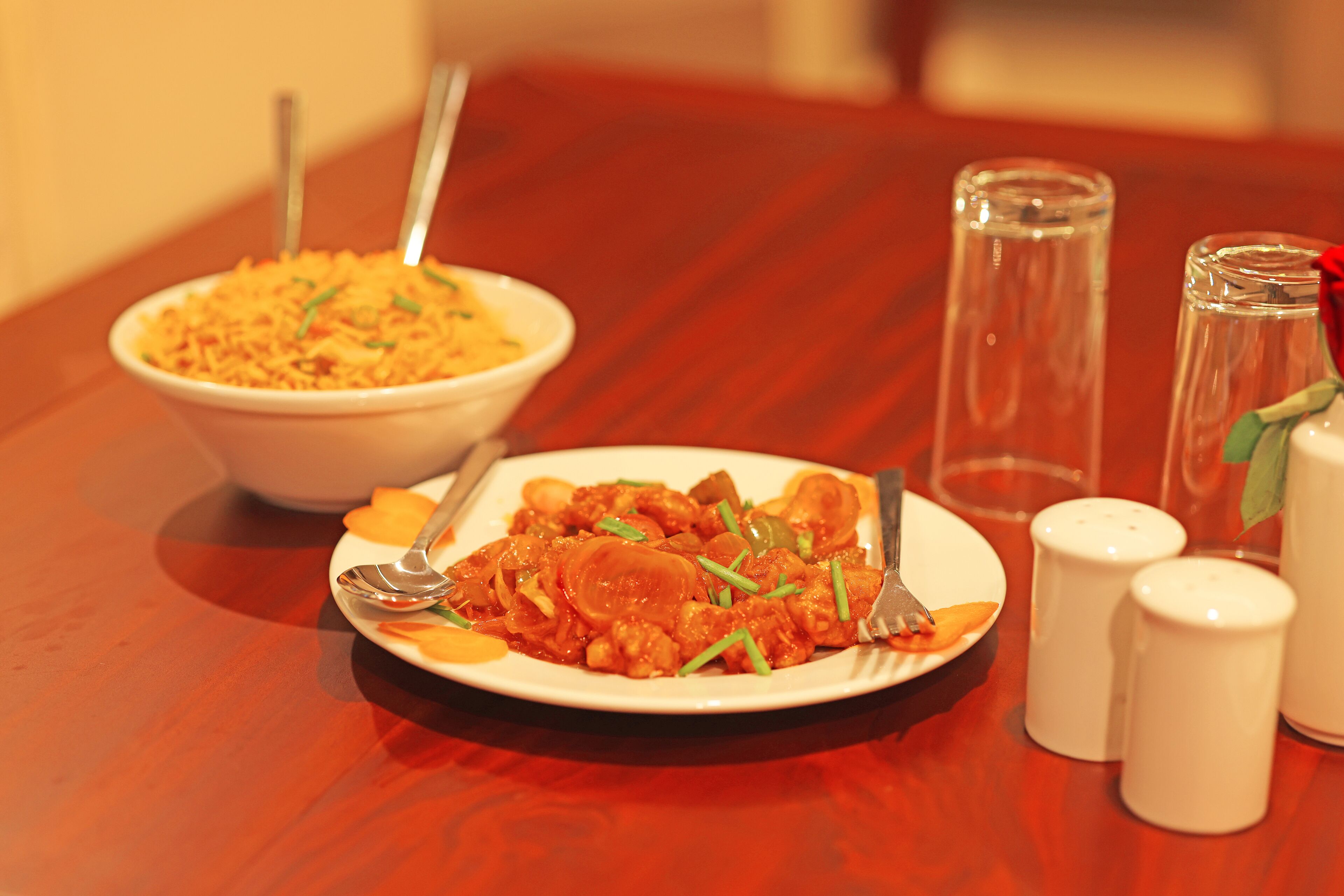 A dining table with a plate of food, a bowl of rice, salt and pepper shakers, and a glass.