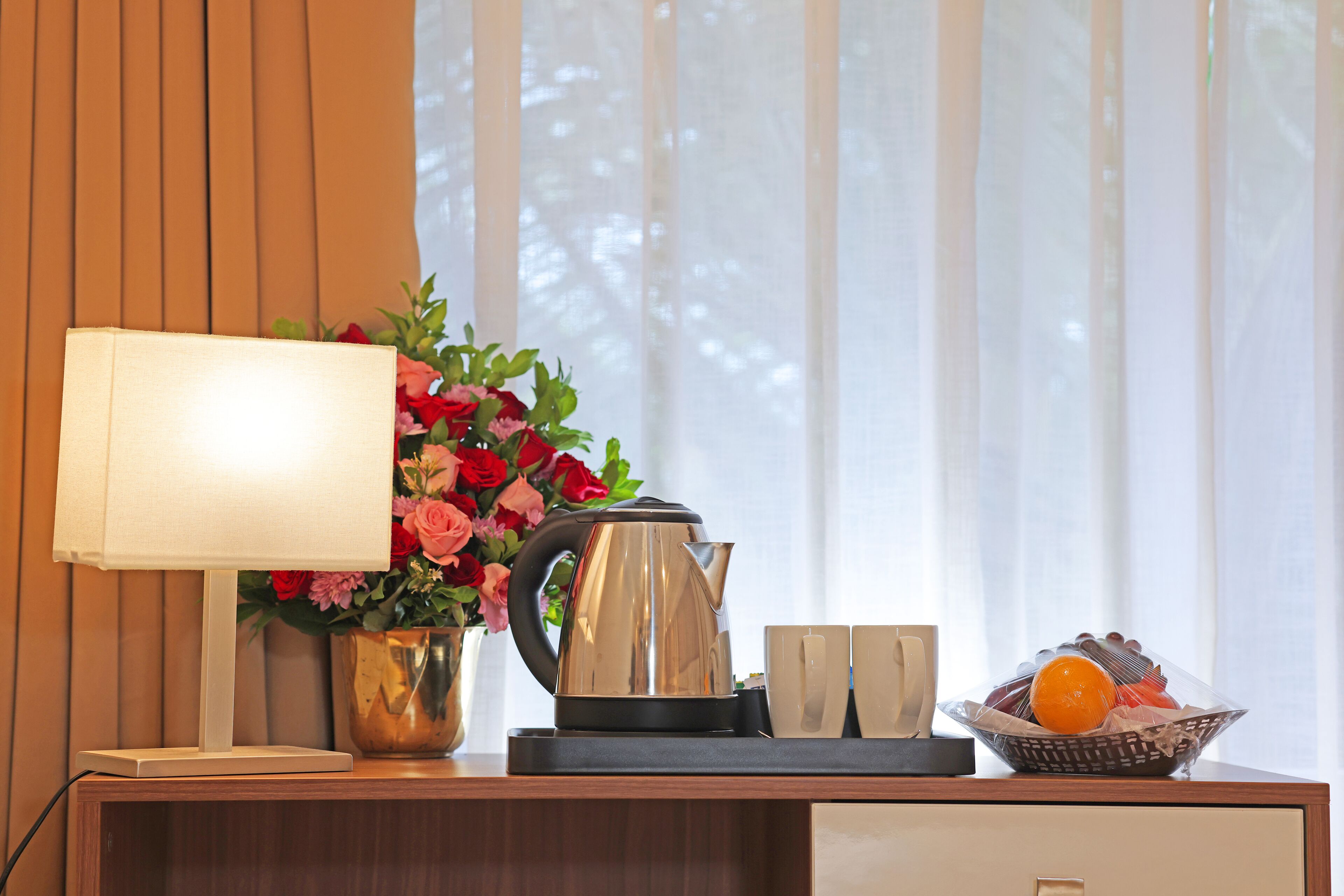 Ein Holztisch mit einer Lampe, einem Blumenstrauß, einem Wasserkocher und einer Obstschale.