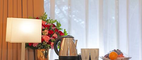 A wooden desk with a lamp, a vase of flowers, a kettle, and a fruit bowl.