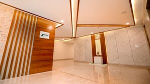 Un hall d’entrée moderne avec un comptoir d’accueil en bois, un mur orné d’un motif géométrique et un sol carrelé.