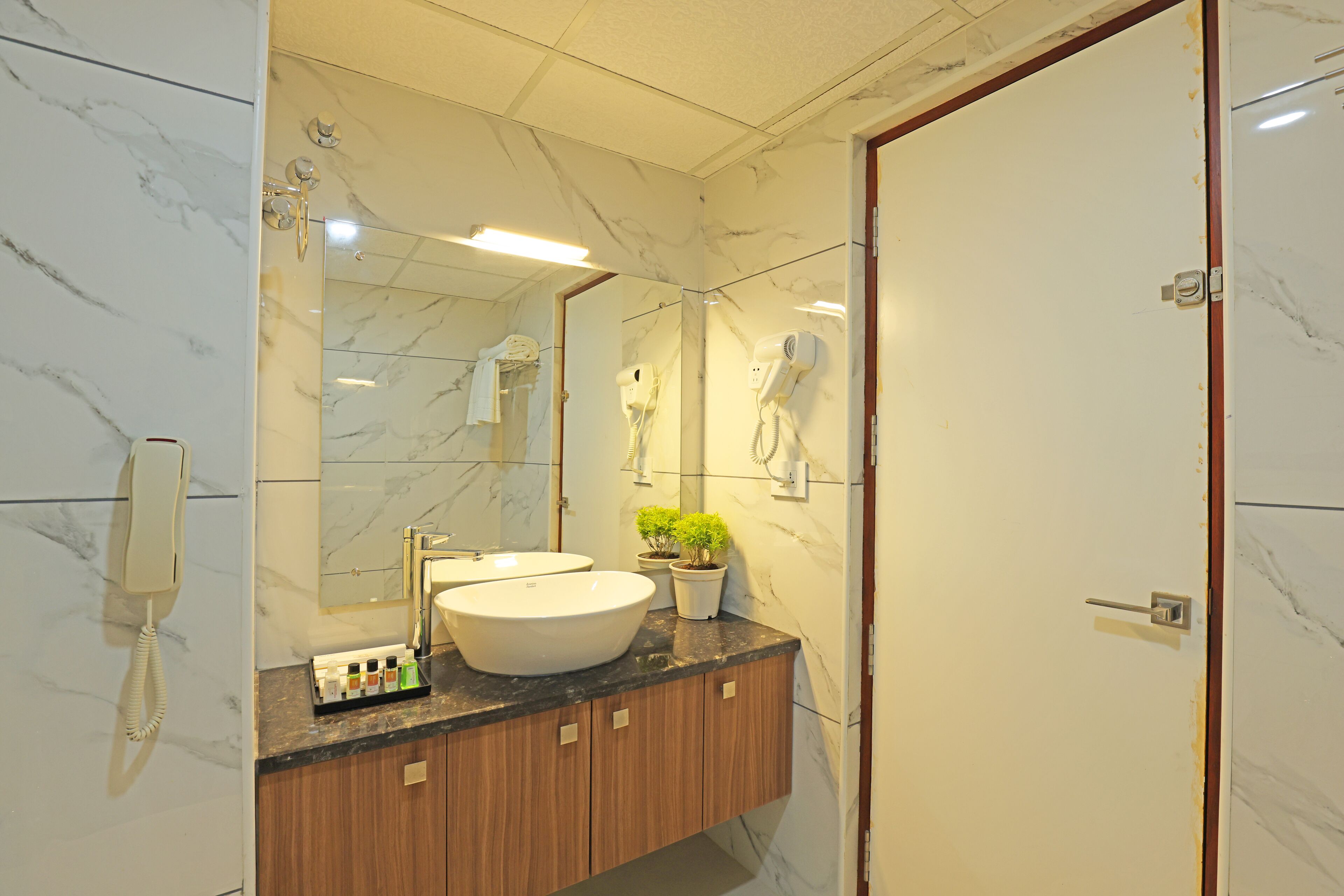 Une salle de bain avec un mur en marbre, un lavabo, un miroir, un sèche-cheveux et un téléphone.