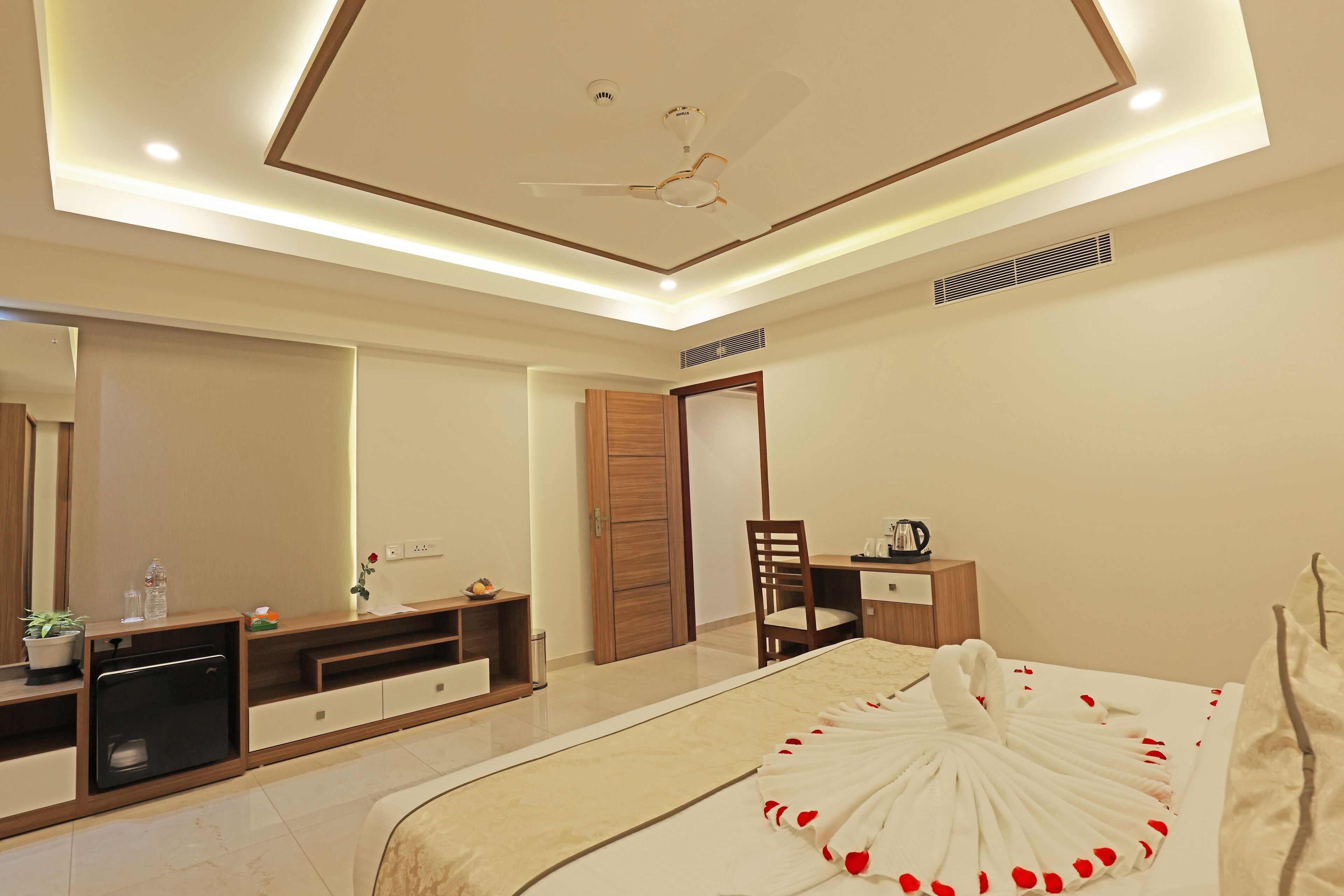 Une chambre à coucher moderne, équipée d’un lit, d’un bureau, d’une chaise, d’un miroir et d’un ventilateur de plafond.