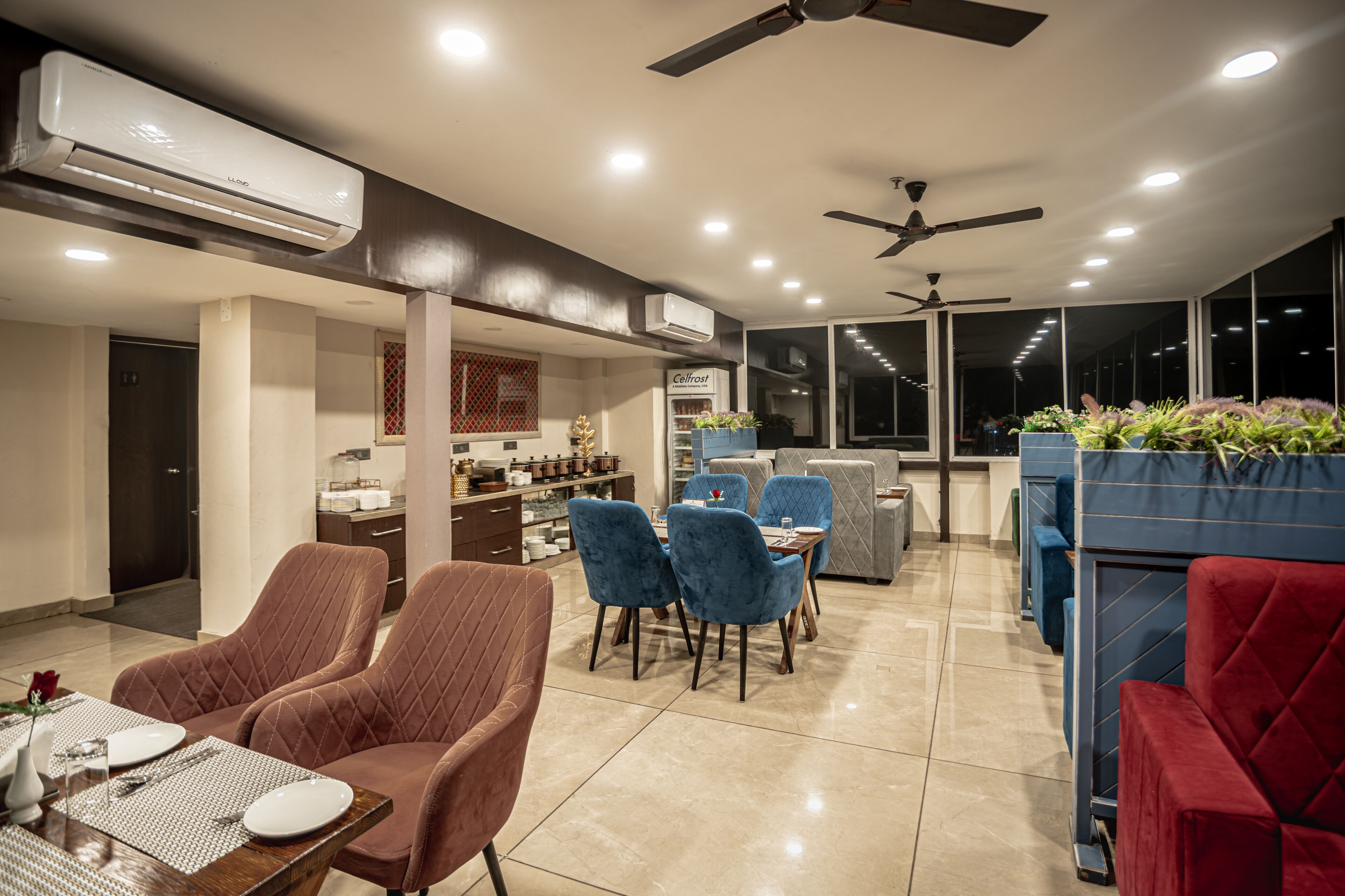A modern dining area with a table set for two, blue and red upholstered chairs, and a ceiling fan.