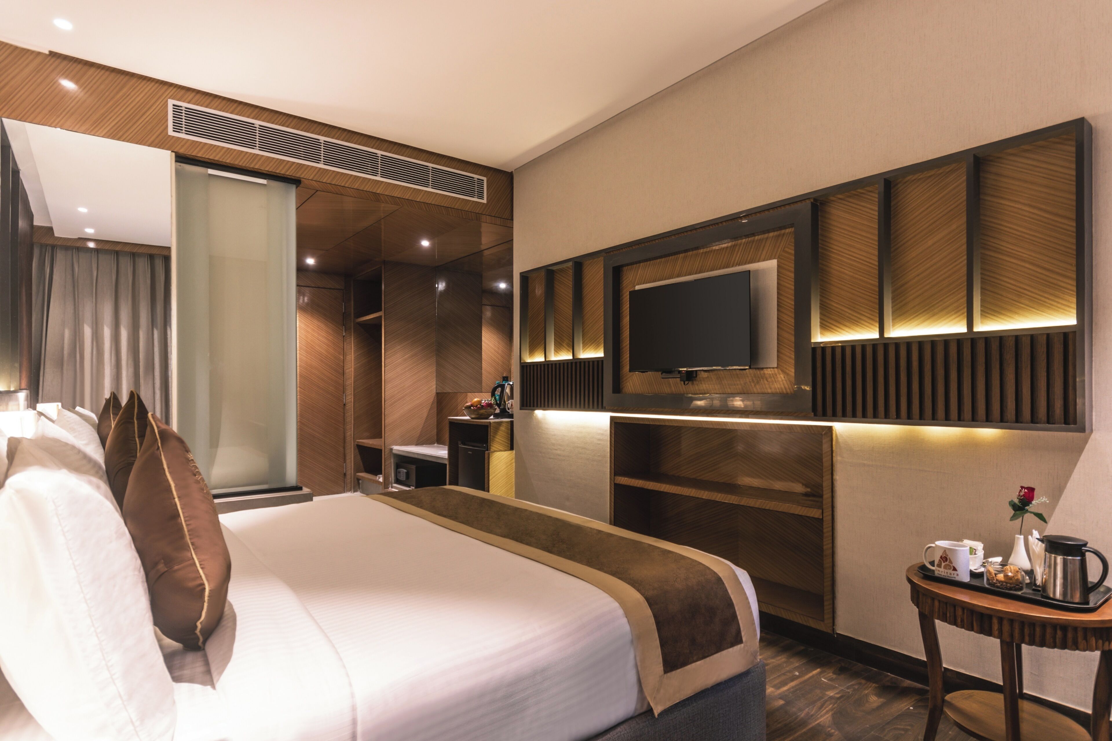 Habitación de hotel con una cama grande, un televisor de pantalla plana montado en la pared, una mesita con una cafetera y un escritorio con una computadora.