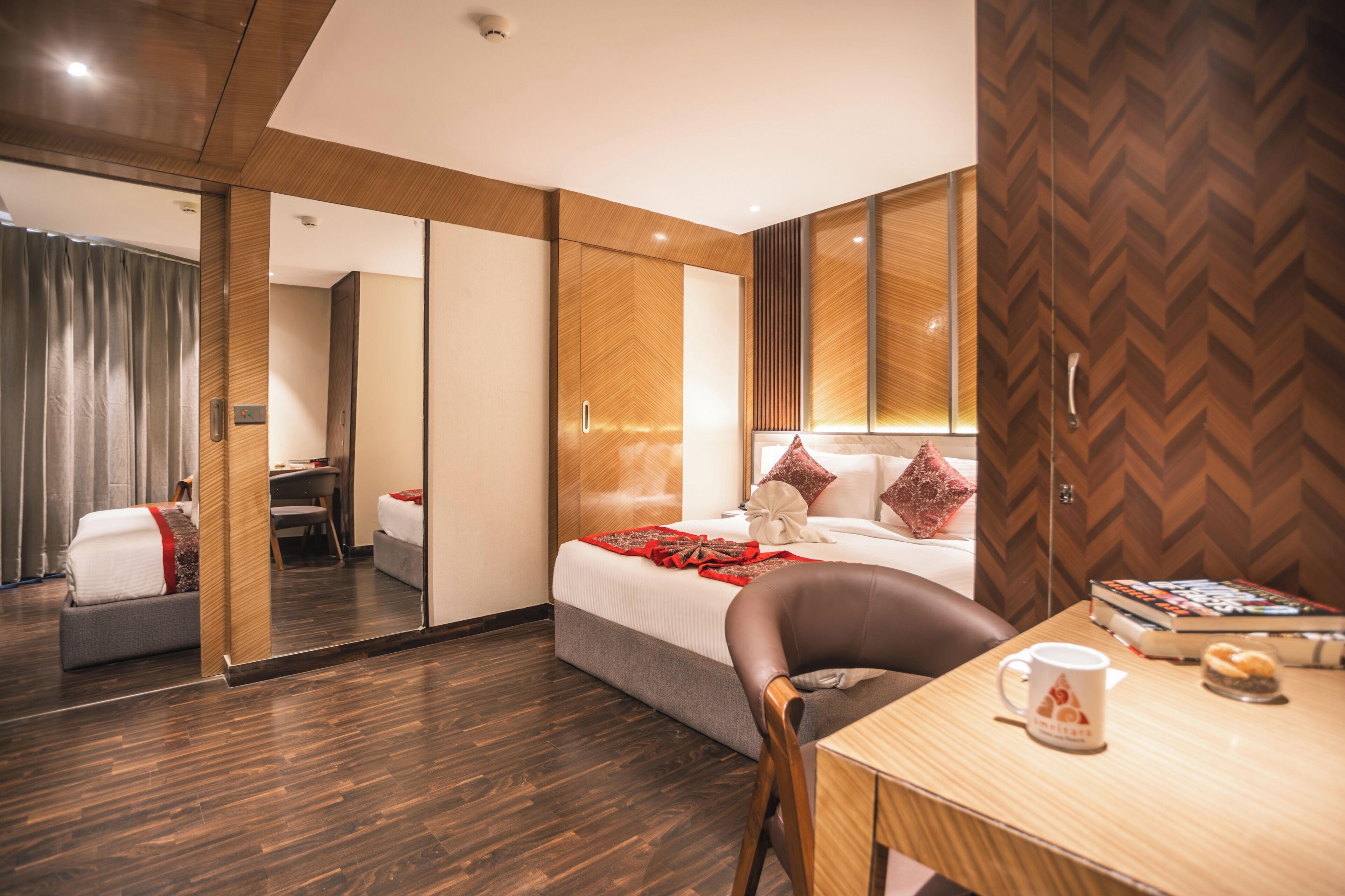 A modern hotel room with a large bed, a desk, a chair, and a mirror.