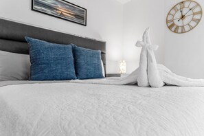 Een netjes opgemaakt bed met een witte deken, twee blauwe kussens en een witte handdoek.