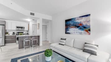 Un salon moderne avec un canapé blanc, une table basse en verre et un tableau accroché au mur.