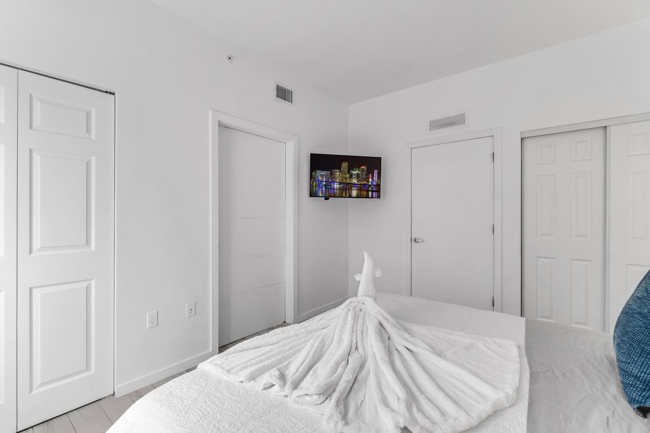 A bedroom with a bed, white walls, and a cityscape painting on the wall.