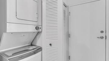 Un lavadero con lavadora y secadora Whirlpool, una puerta blanca y un armario con puertas persianas.