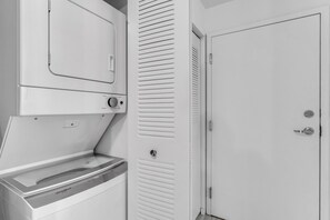 Een wasserij met een Whirlpool wasmachine en droger, een witte deur en een kast met verstelbare luiken.