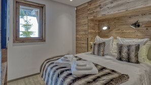 Een moderne slaapkamer met een houten paneelwand, een groot raam, een bed met witte lakens en een bontdeken.