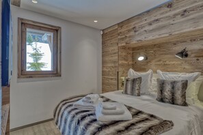 Un dormitorio moderno con un panel de madera en la pared, un ventanal grande, una cama con ropa blanca y un plaid de piel.
