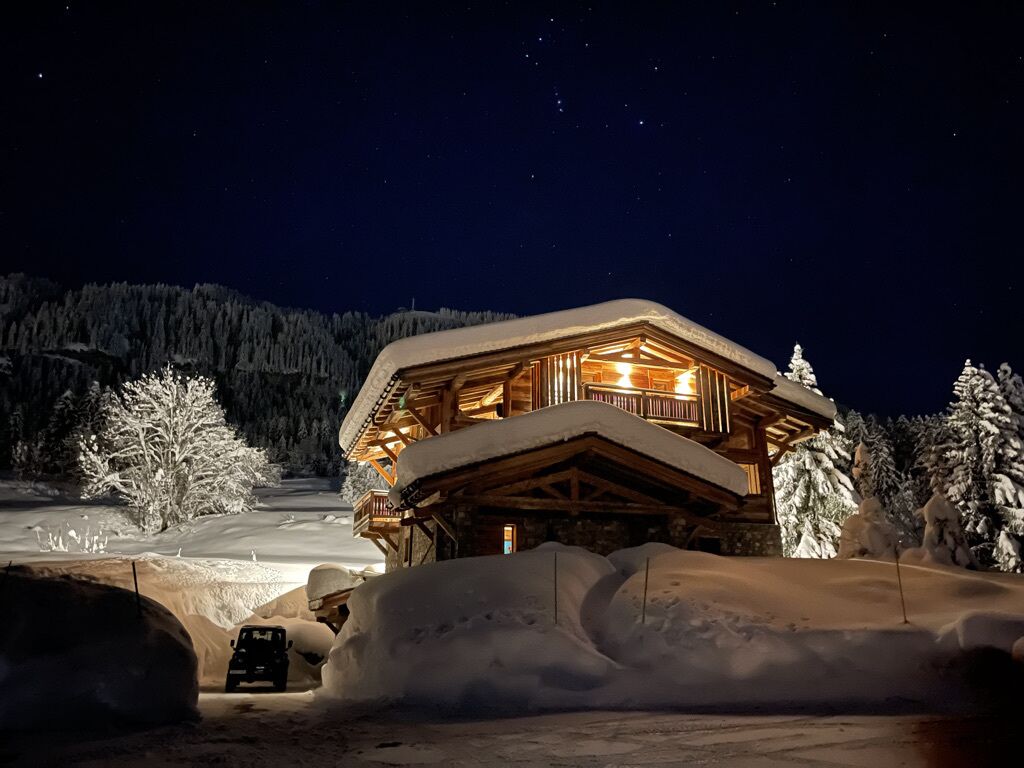 Un rifugio coperto di neve con facciata in legno e un balcone, circondato da alberi innevati e un cielo notturno sereno.