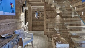 Een modern interieur met houten wanden, een glazen trap, een witte stoel en een televisie met daarop een scène van het skiën.