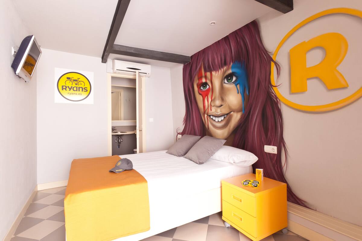 Quarto de hotel com uma cama, mesa de cabeceira, televisão fixada na parede e porta para o banheiro.