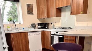 Une cuisine avec des meubles en bois, un lave-vaisselle, un four à micro-ondes, une cuisinière à gaz et un tabouret de bar violet.
